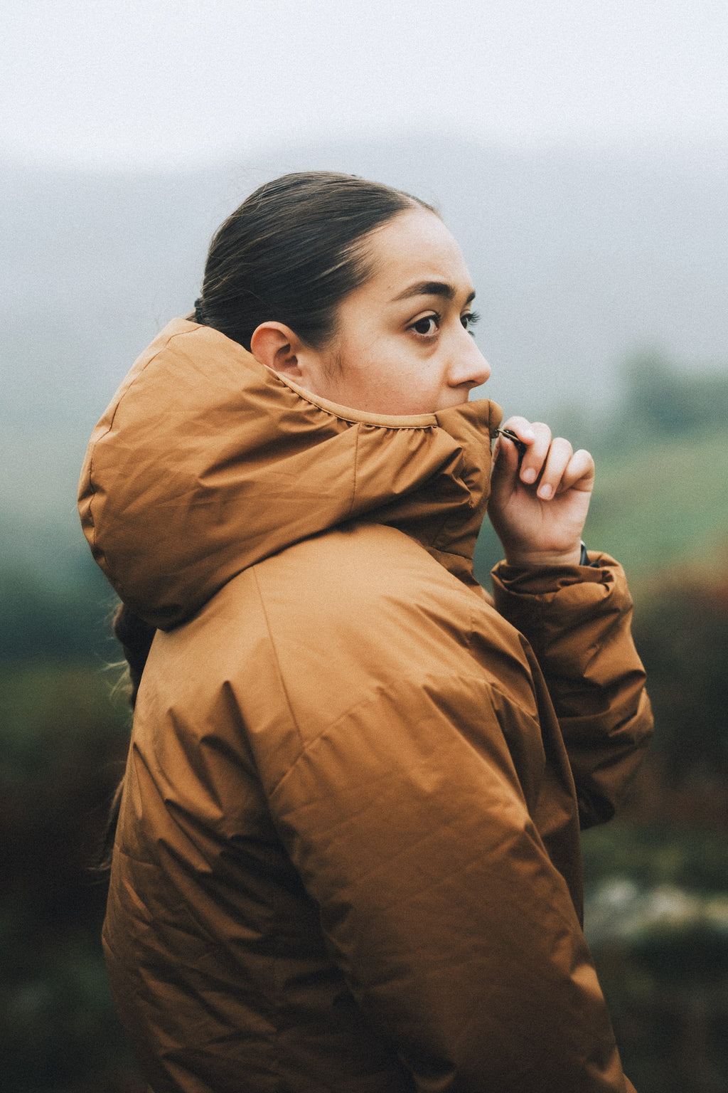 Close-up of a woman adjusting the high collar of her orange insulated jacket, to provide protection in cold conditions.