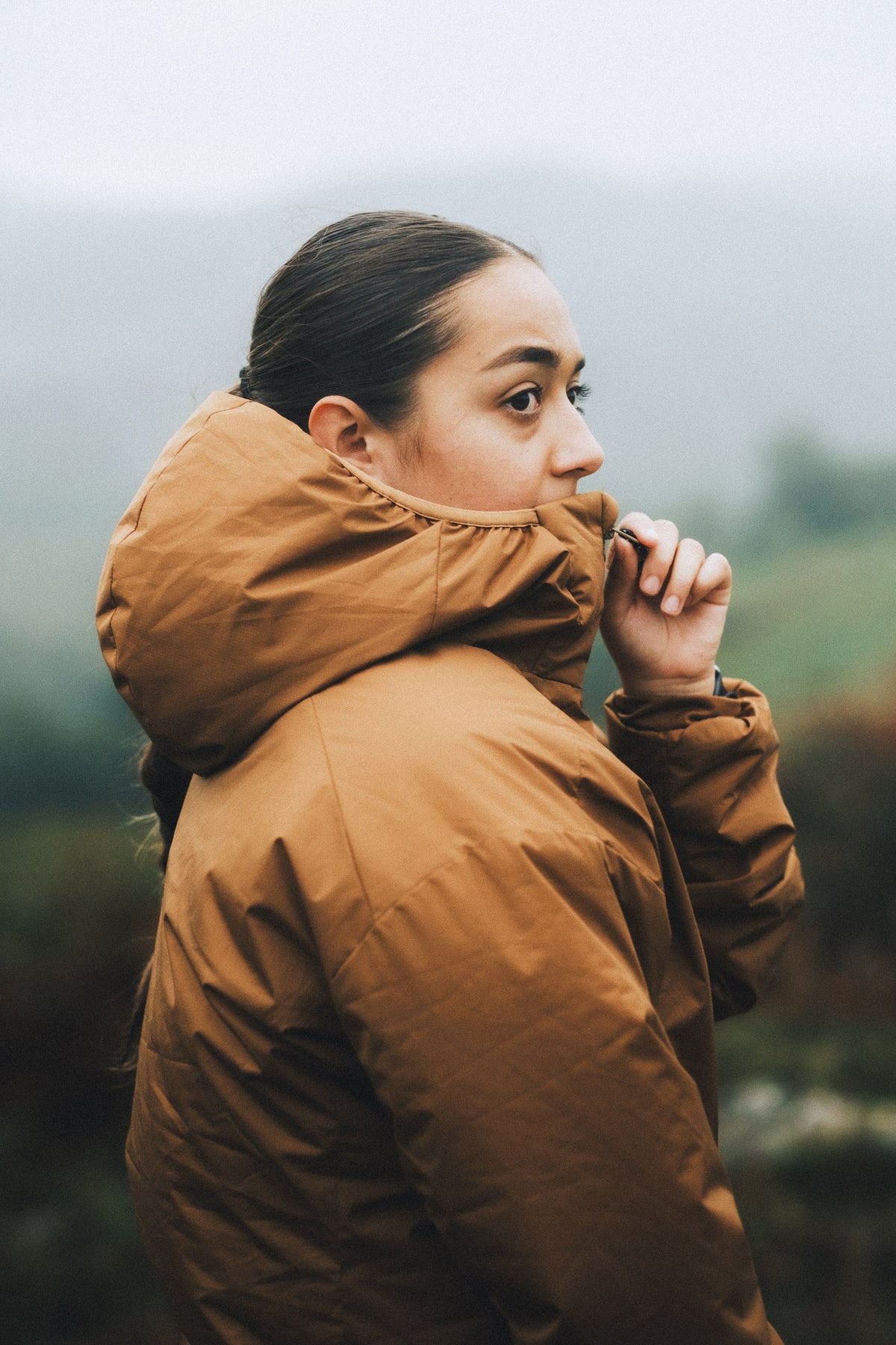 Close-up of a woman adjusting the high collar of her orange insulated jacket, to provide protection in cold conditions.