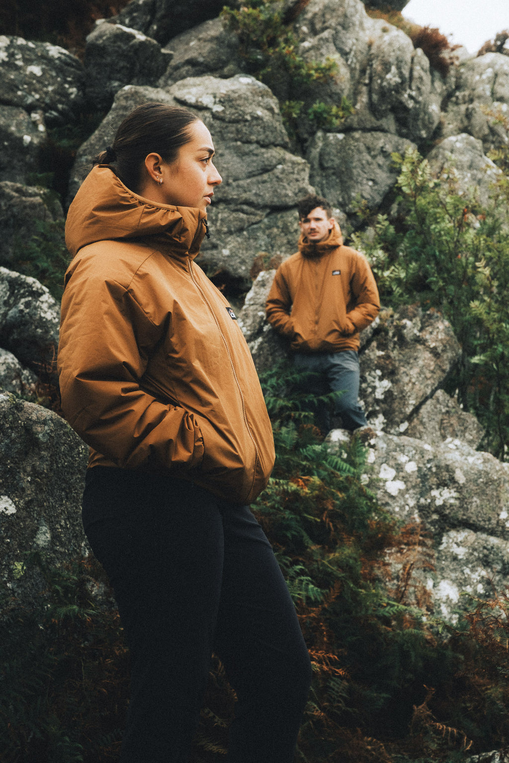 Two climbers wearing orange insulated jackets on rocky mountain terrain, showcasing the jackets’ fit and freedom of movement.